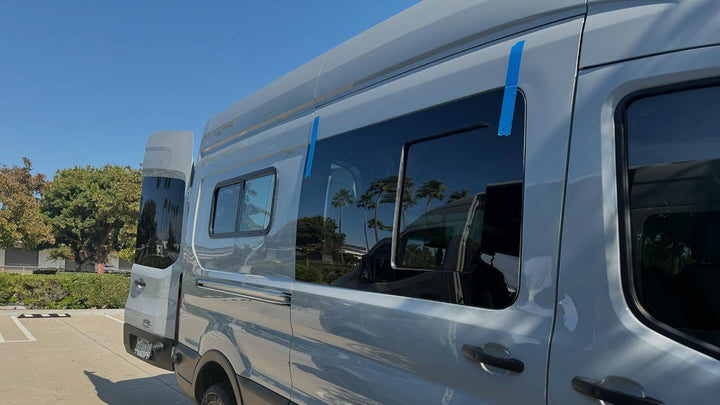 Silver van with reflective windows in a parking lot with trees in the background