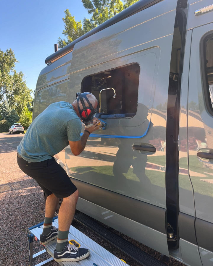 Person working on a vehicle window with protective gear outdoors